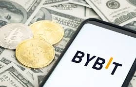 Logo da corretora Bybit exibido em smartphone sobre cédulas de dólar e criptomoedas, simbolizando negociação de ativos digitais"