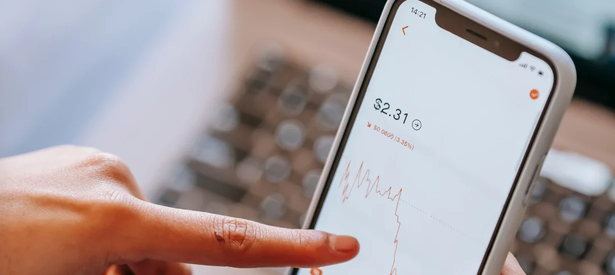 dedo tocando celular com uma tela de trader e fundo branco.
