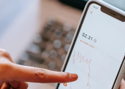 dedo tocando celular com uma tela de trader e fundo branco.