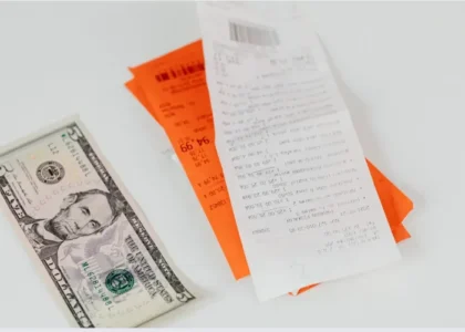 Nota fiscal ao lado de cédula de cinco dólares americanos sobre superfície branca