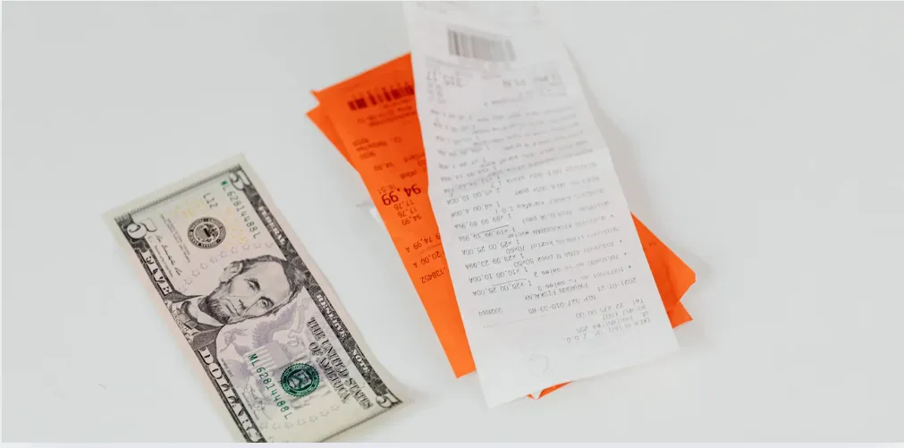 Nota fiscal ao lado de cédula de cinco dólares americanos sobre superfície branca