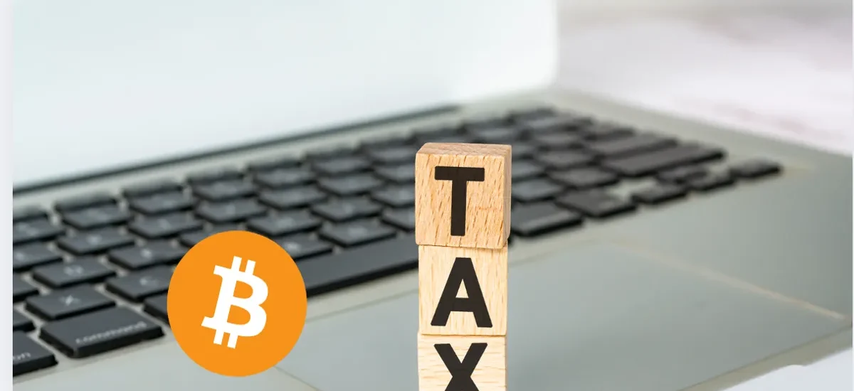 Blocos de madeira com a palavra TAX e símbolo do Bitcoin sobre teclado de notebook, representando impostos e regulamentação em criptomoedas