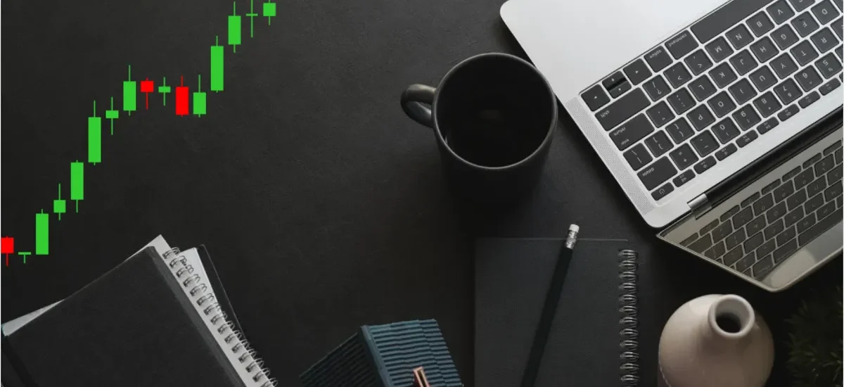 Candlesticks de Bitcoin em tendência de alta ao lado de notebook e caderno sobre mesa preta