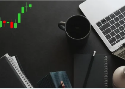 Candlesticks de Bitcoin em tendência de alta ao lado de notebook e caderno sobre mesa preta