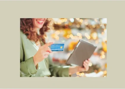 Mulher sorridente segura um cartão de crédito azul e um tablet, representando praticidade e segurança nas compras online com carteiras digitais.